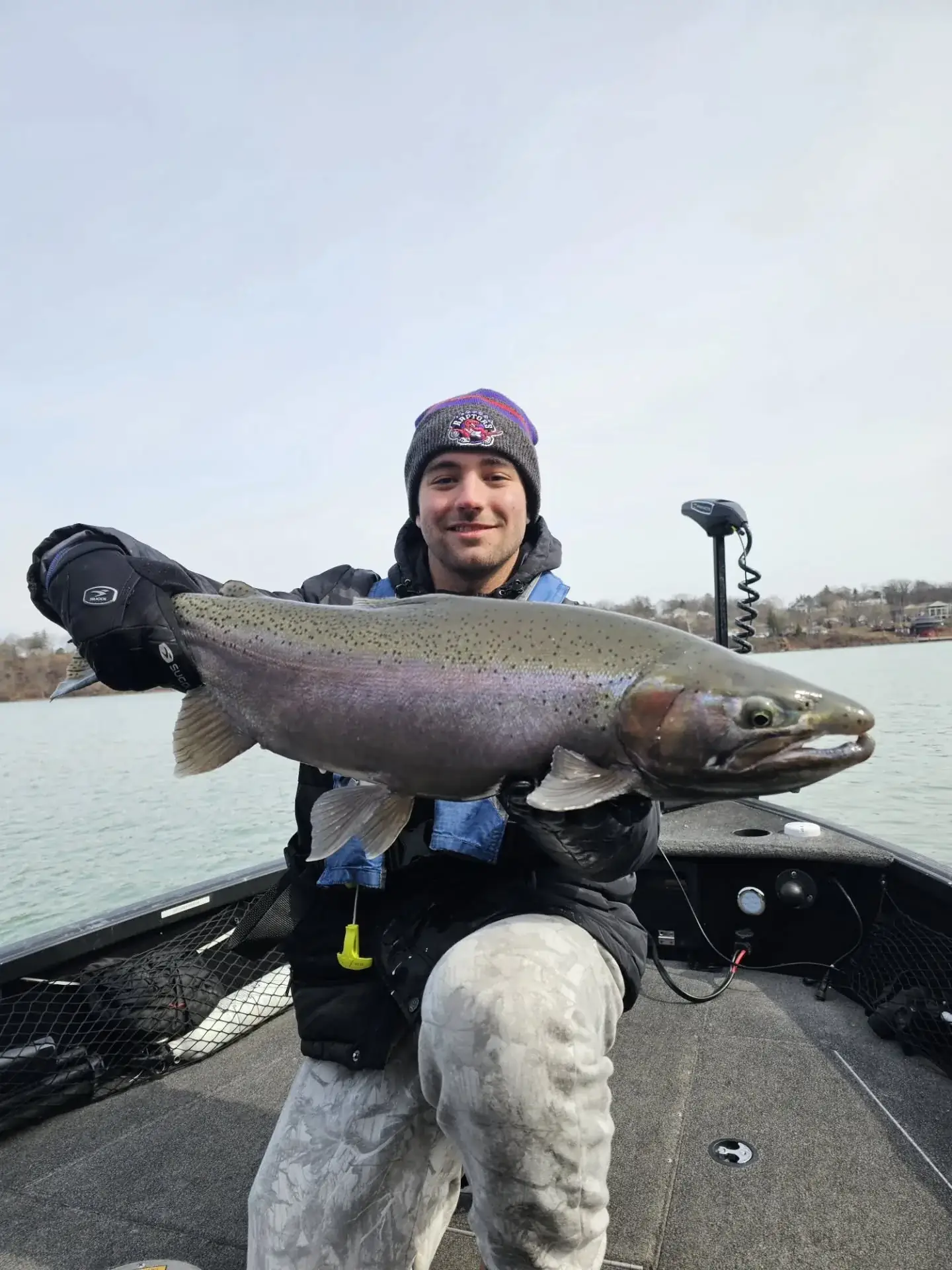 Angler holding a large steelhead aboard the river boat under a cold grey sky