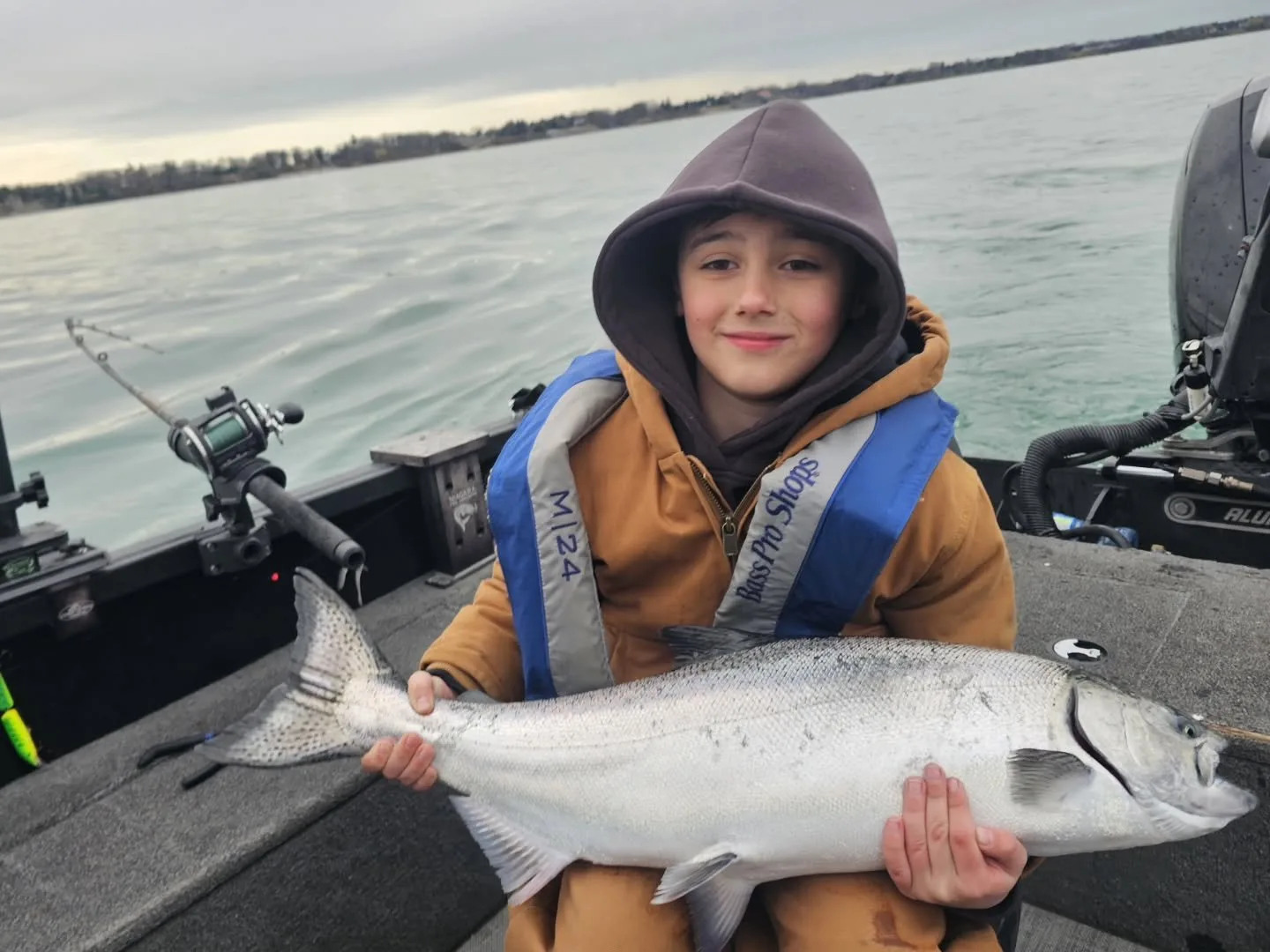 A young angler holding a chinook salmon aboard the open aluminum boat