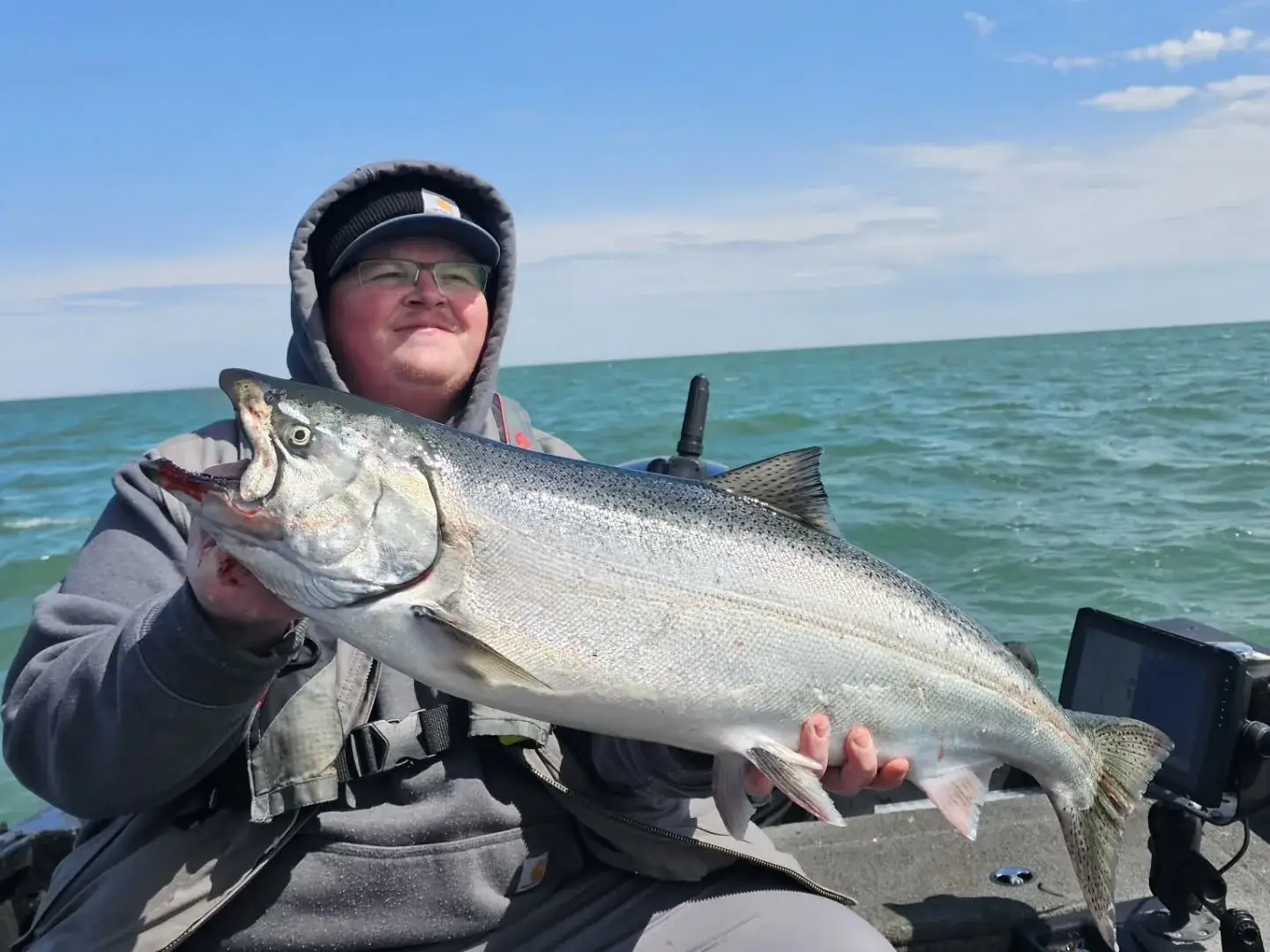 Angler holding a chinook salmon aboard the open boat on open water