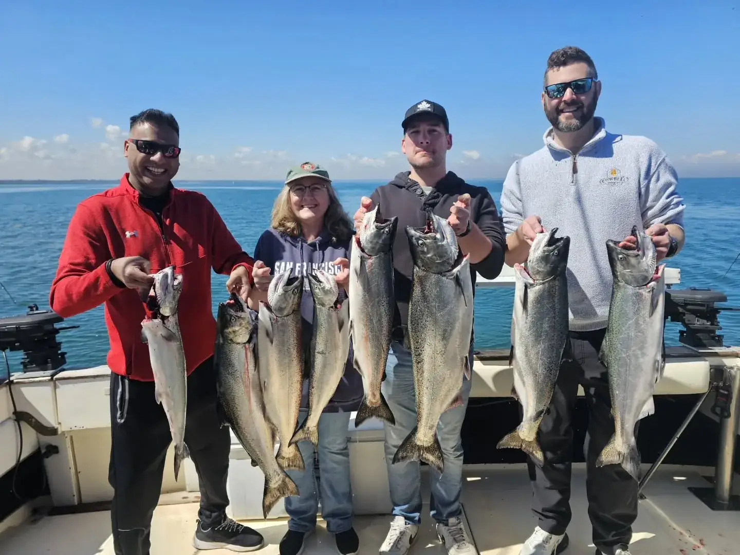Four anglers on a King Slayer charter boat holding chinook salmon over open water