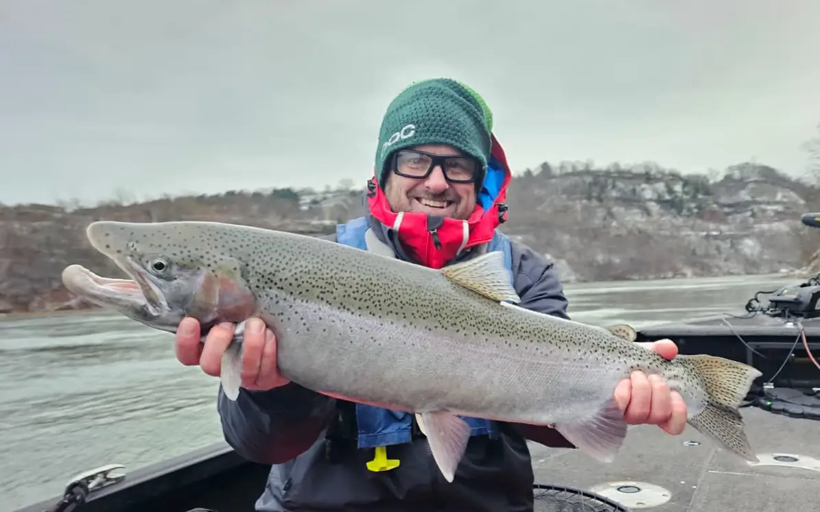 Angler holding a steelhead with the snow-dusted Niagara gorge walls behind