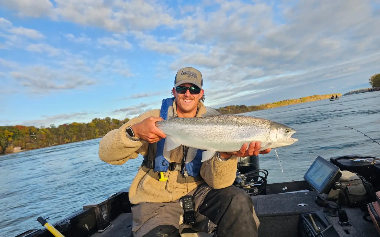 Angler holding a bright steelhead under a blue sky on the lower Niagara River