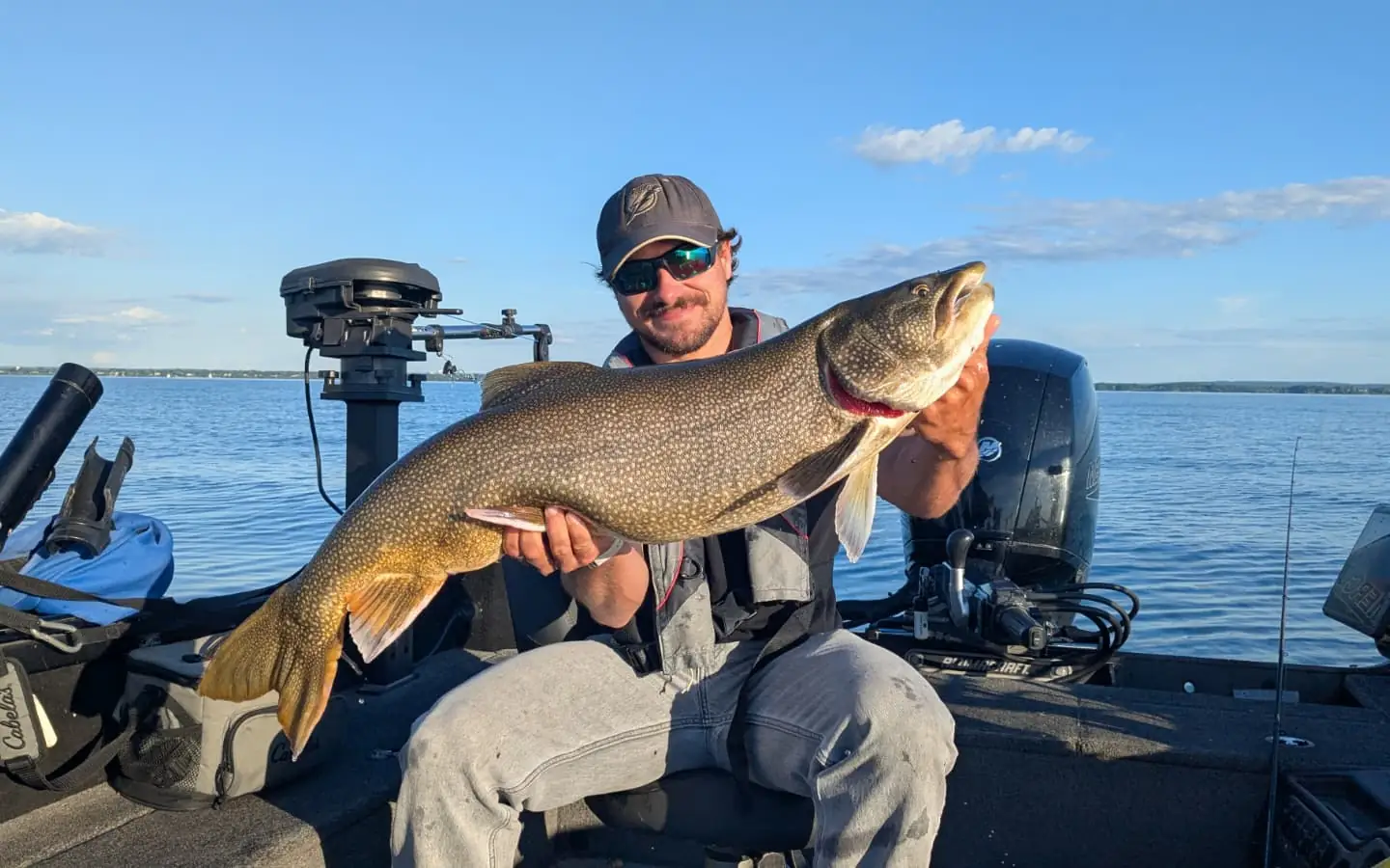 Angler holding a lake trout under a clear sky on Lake Ontario