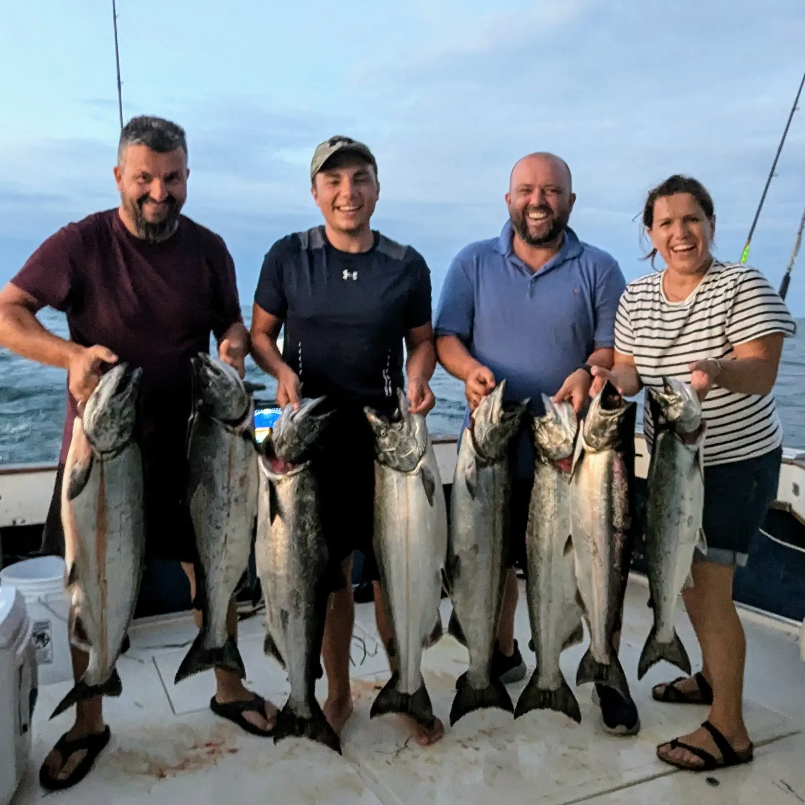 Four anglers on the King Slayer deck holding a row of Lake Ontario chinook salmon